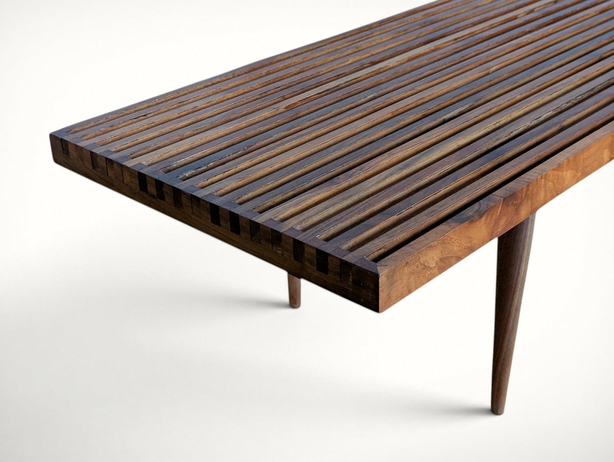 Corner detail of the Smilow bench showing finger joinery, slat ends and a tapered walnut leg