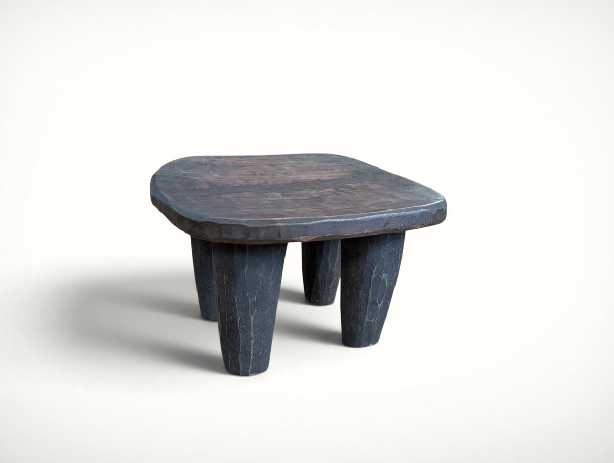 Senufo stool at an angle showing the thick hand-hewn seat edge and faceted adze-textured legs
