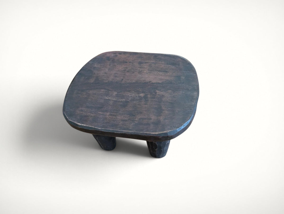 Side view of the small Senufo stool — rustic carved plant stand with a warm dark finish