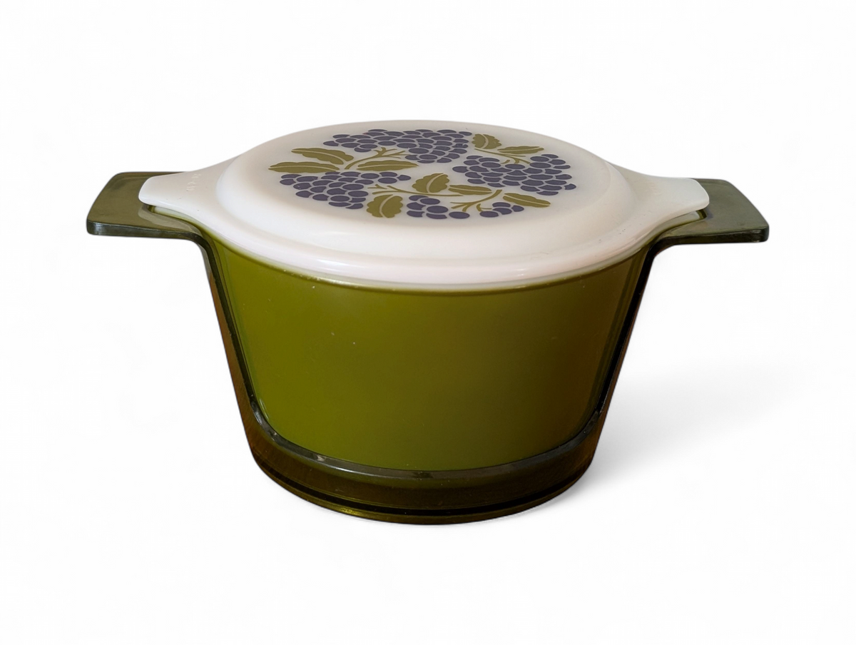 Vintage avocado green one-quart casserole with white opal ware lid featuring a purple grapes pattern and original green glass hugger cradle, 1973
