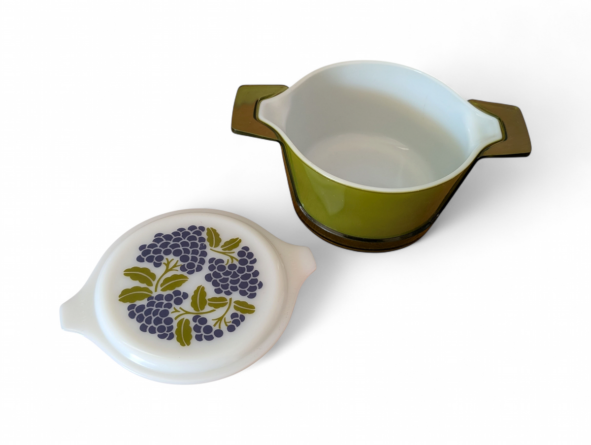 Vintage avocado green one-quart casserole with white opal ware lid featuring a purple grapes pattern and original green glass hugger cradle, 1973