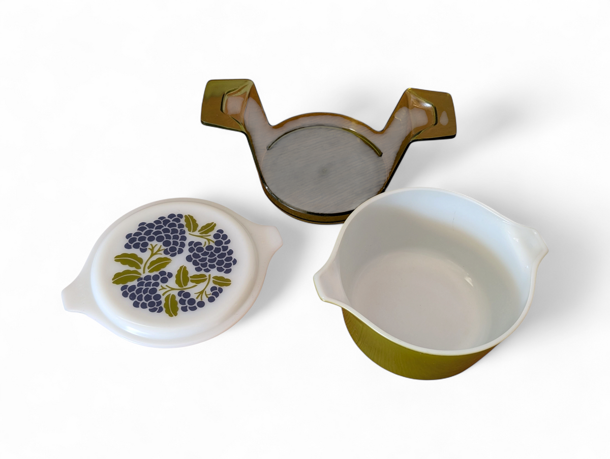 Vintage avocado green one-quart casserole with white opal ware lid featuring a purple grapes pattern and original green glass hugger cradle, 1973