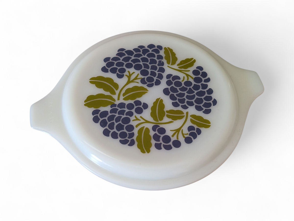 Vintage avocado green one-quart casserole with white opal ware lid featuring a purple grapes pattern and original green glass hugger cradle, 1973