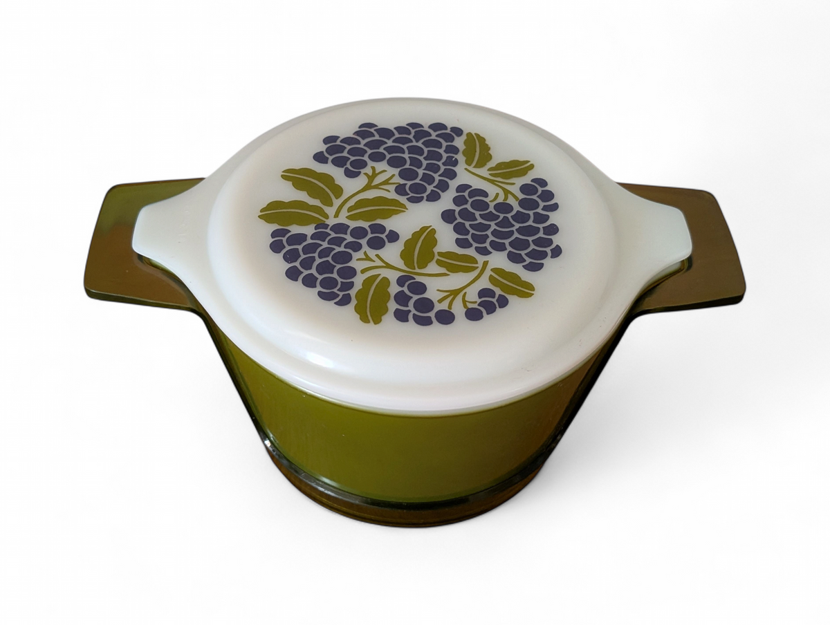 Vintage avocado green one-quart casserole with white opal ware lid featuring a purple grapes pattern and original green glass hugger cradle, 1973
